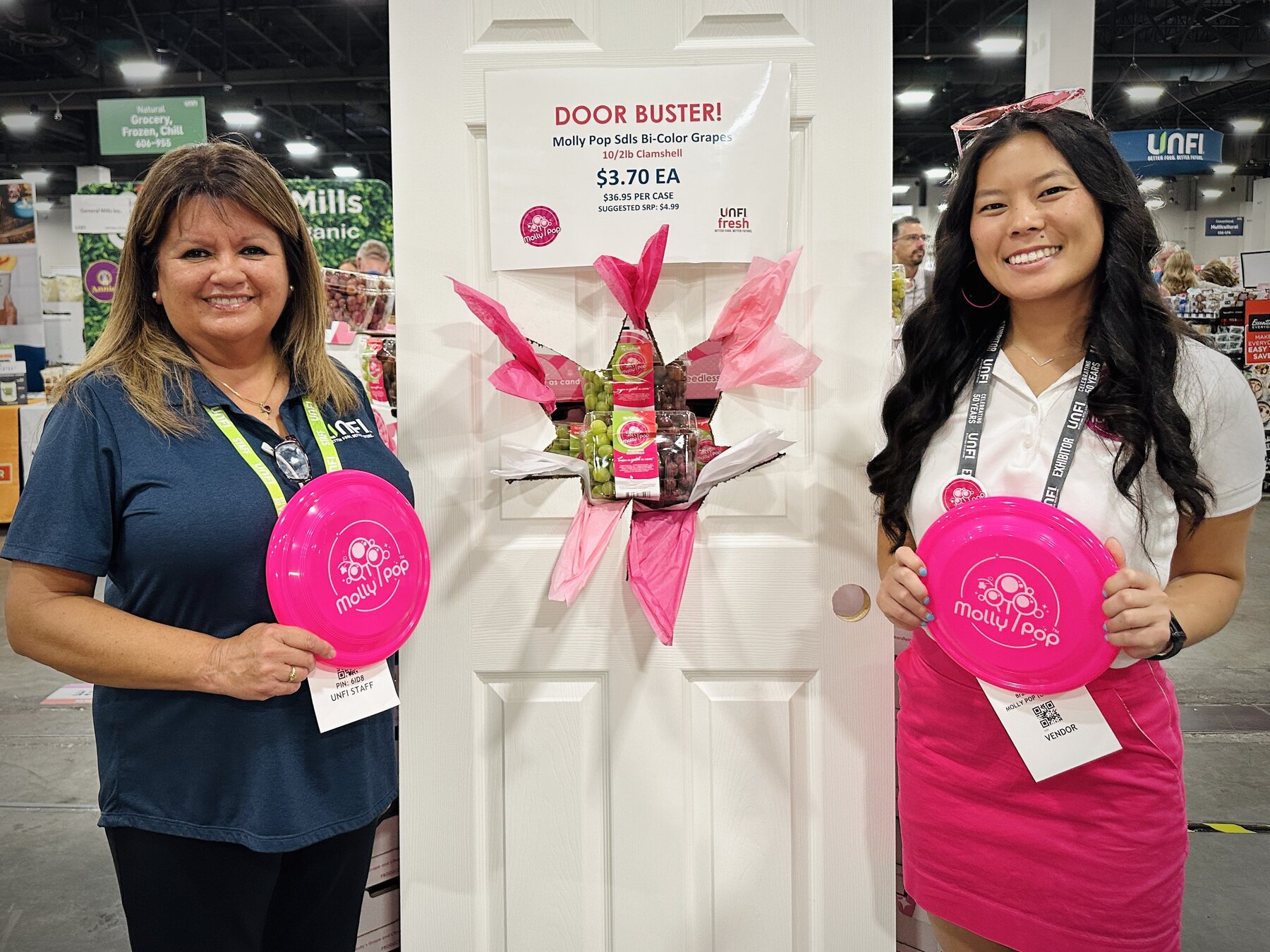 UNFI show attendees with Molly Pop pink discs beside the grape door-buster display